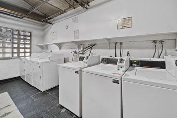 A clean, white industrial room with a row of washing machines on the wall.